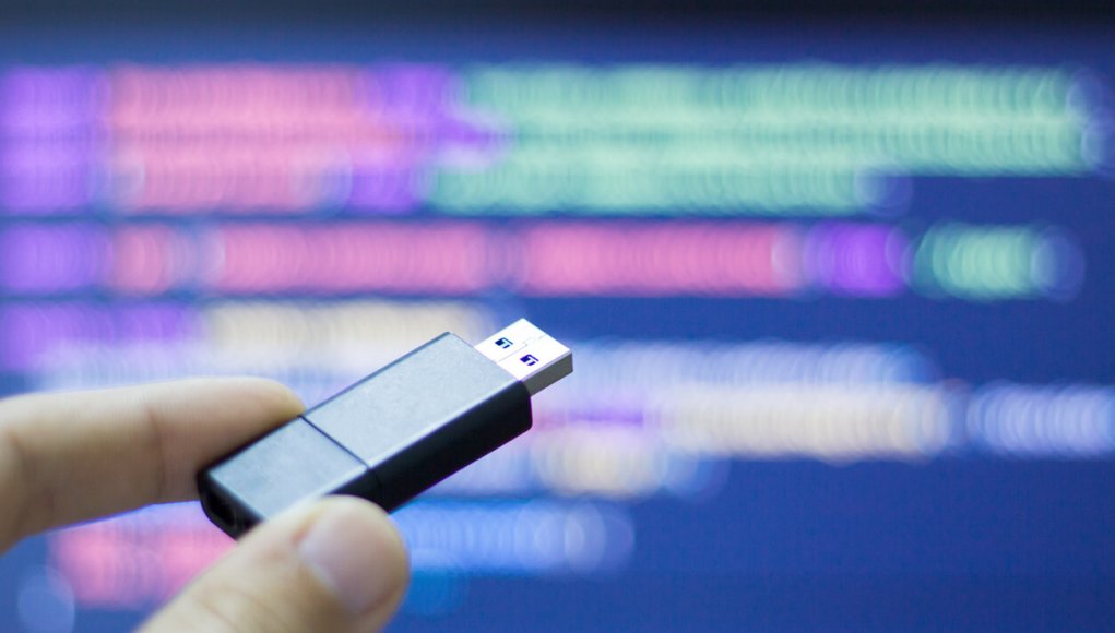 Thumb drive against pink and green computer code. Purple background.