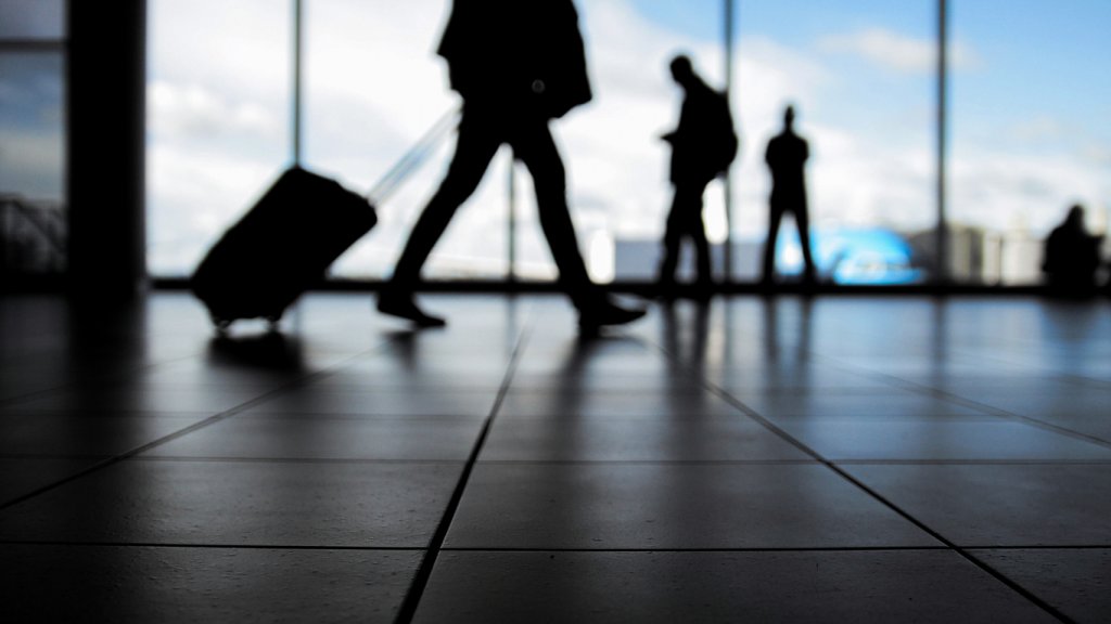 Travelers in airport walking to departures by escalator in front of window, silhouette, blue colors