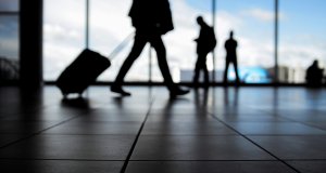 Travelers in airport walking to departures by escalator in front of window, silhouette, blue colors