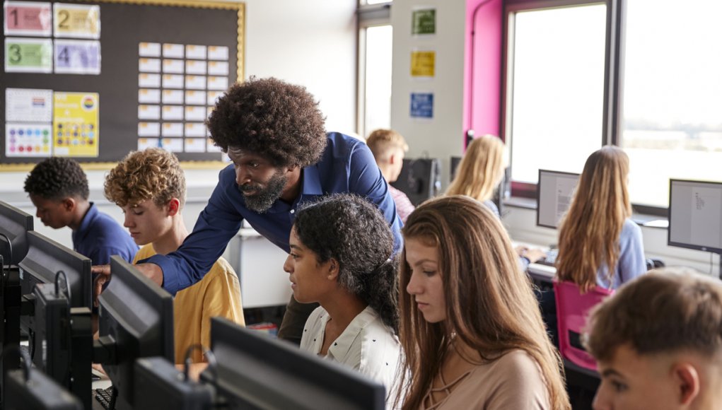 Teacher Helping Teenage Female High School Student Working In Computer Class