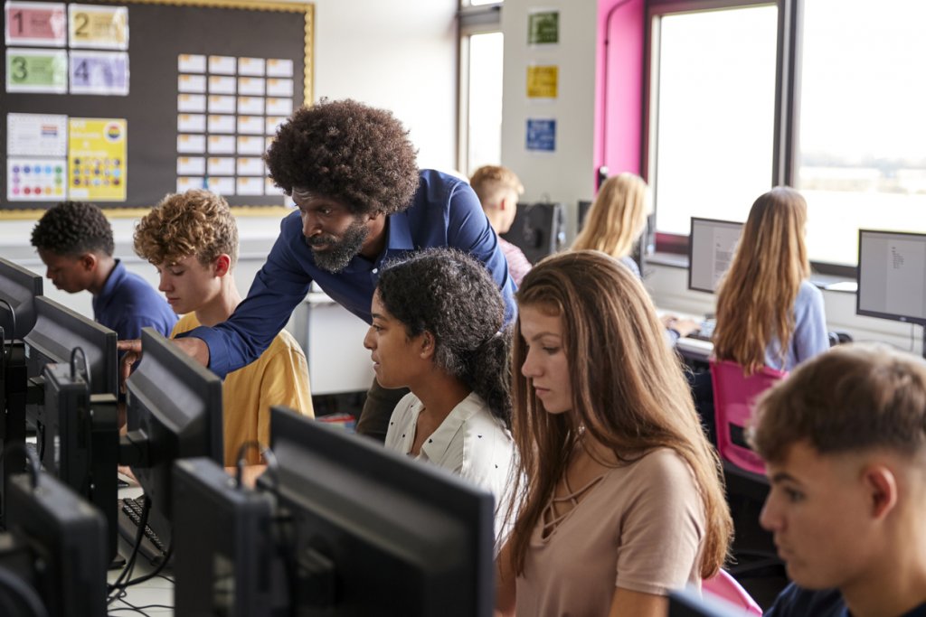 Teacher Helping Teenage Female High School Student Working In Computer Class