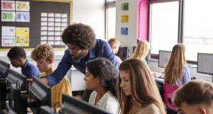 Teacher Helping Teenage Female High School Student Working In Computer Class