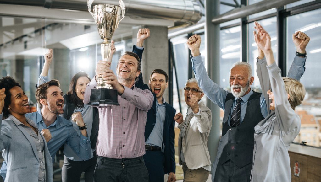 Large group of cheerful business people celebrating success with a trophy in the office.