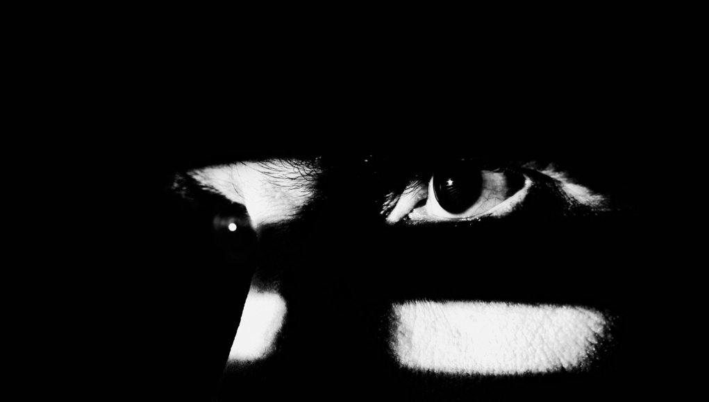 Close up of a male face illuminated through a window blind. Focus on the eye, High contrast.