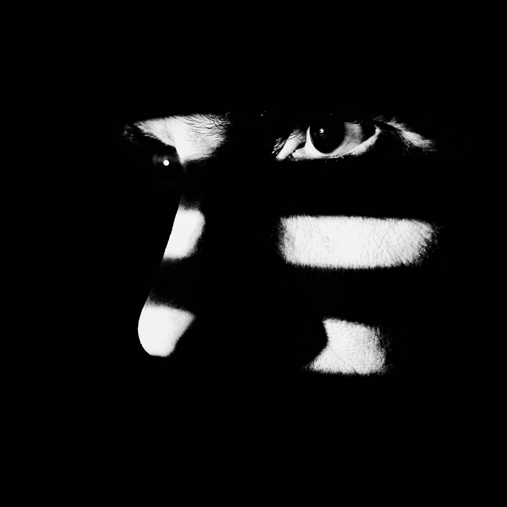 Close up of a male face illuminated through a window blind. Focus on the eye, High contrast.