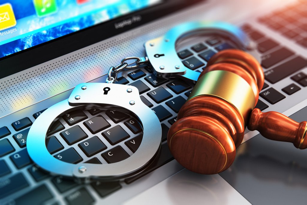 Creative abstract cyber crime, online piracy and internet web hacking concept: 3D render illustration of the macro view of metal handcuffs and wooden judge mallet, gavel or hammer on laptop notebook computer keyboard with selective focus effect