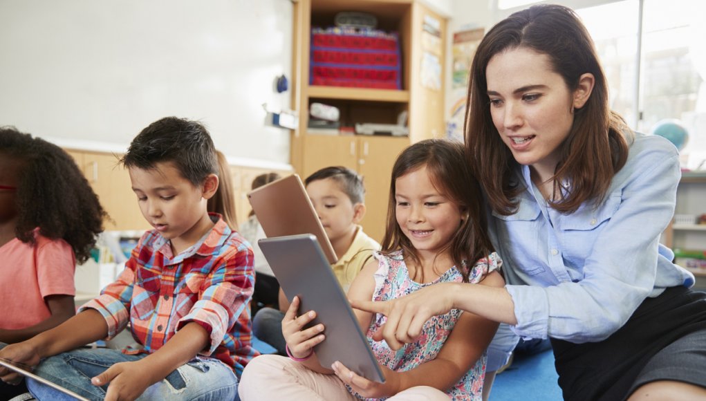 Teacher helps girl in elementary class with tablet computers