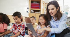 Teacher helps girl in elementary class with tablet computers