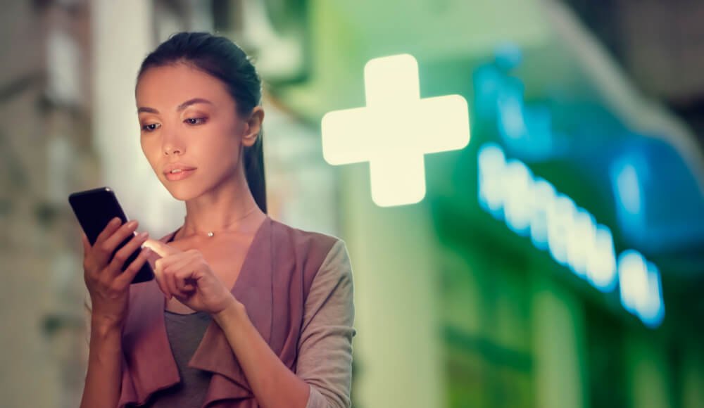 Woman in front of pharmacy, on mobile phone, during pandemic