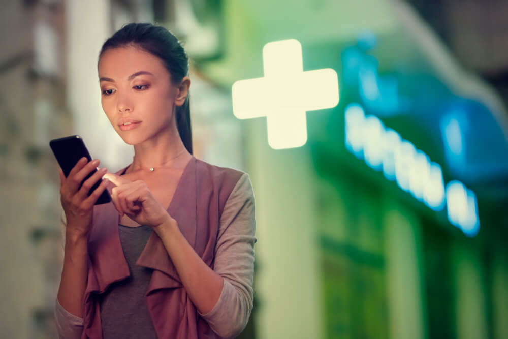 Woman in front of pharmacy, on mobile phone, during pandemic